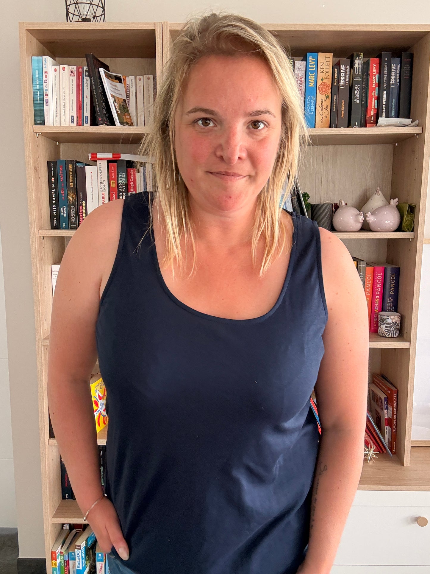 Femme portant un débardeur bleu marine uni et confortable, debout devant une bibliothèque.