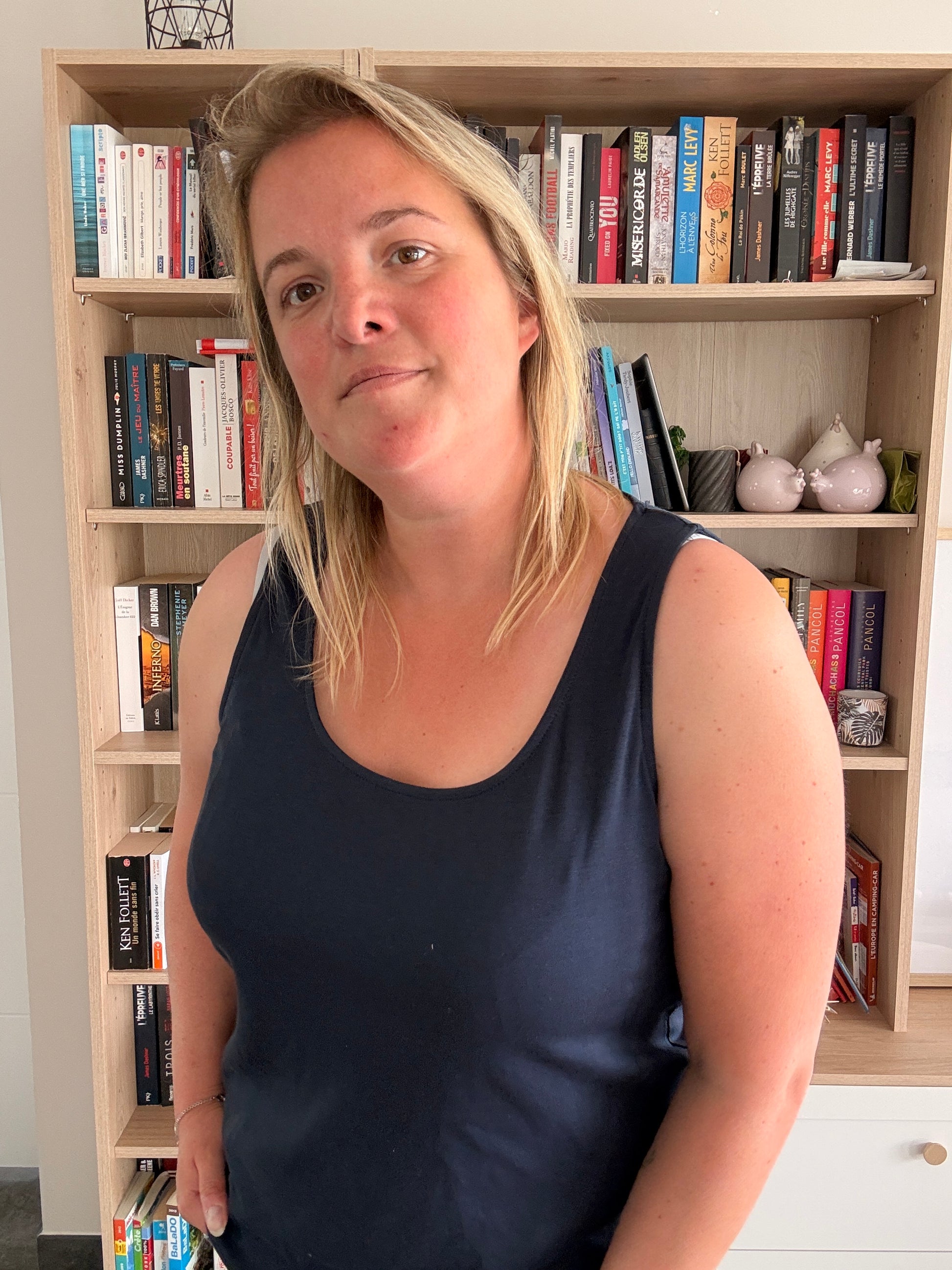 Homme? Non. Une femme portant un débardeur bleu marine uni et confortable debout devant une étagère remplie de livres.