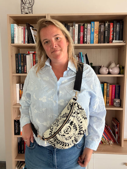 Homme portant un sac banane floral noir et blanc légère et pratique contre fond bibliothèque.