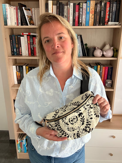 Femme tenant un sac banane floral noir et blanc, léger et pratique, posé sur le ventre, en intérieur devant une bibliothèque.