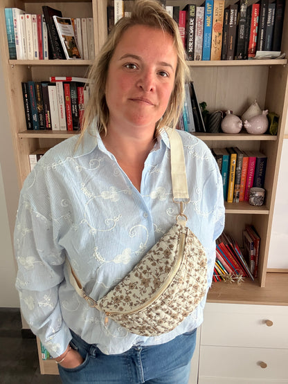 Sac banane femme fleuri taupe avec fond ivoire porté en travers, bandoulière réglable et zip doré.