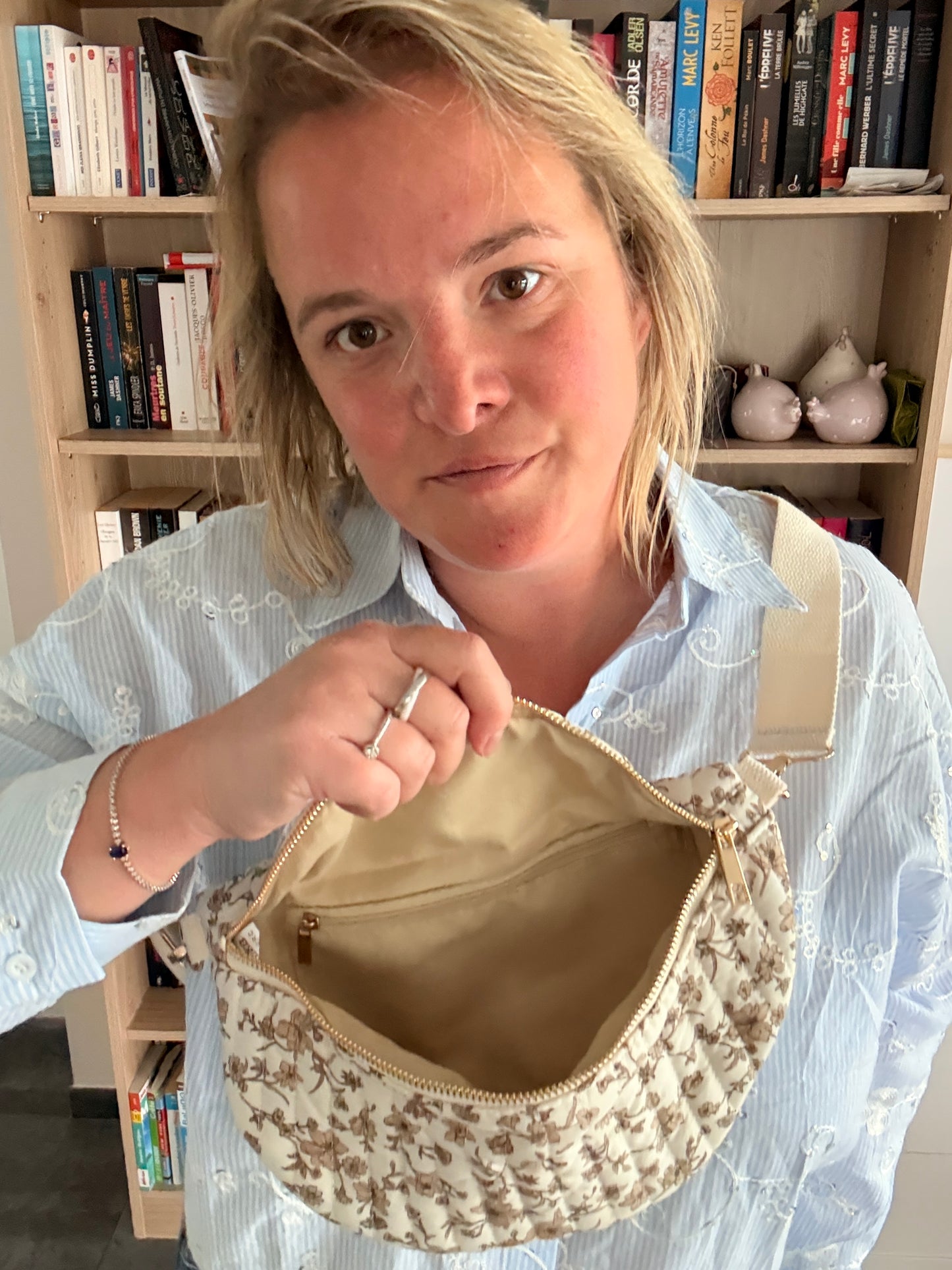 Sac Banane Femme Fleuri Taupe Fond Ivoire – Zip Doré & Bandoulière Réglable: femme montrant l’intérieur beige d’une banane à fleurs taupe, fermée par zip doré.