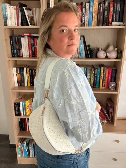 Sac banane femme en broderie anglaise crème portée en bandoulière, près des étagères et livres.