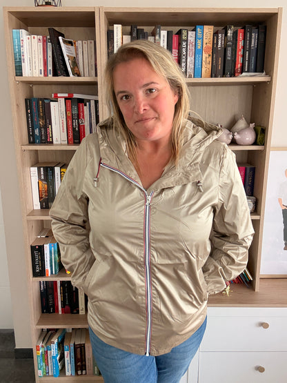 Imperméable mi-saison couleur sable irisée porté par une femme debout devant une bibliothèque.