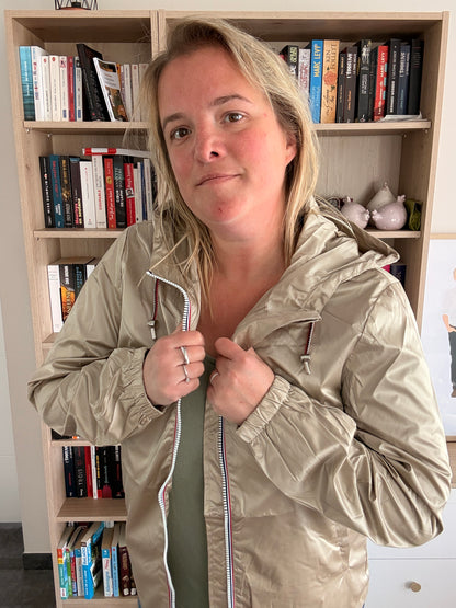 Laura Jo Imperméable Mi-Saison Mi-longue couleur Sable Irisé portée par une femme devant une bibliothèque, capuche et fermeture éclair visibles.