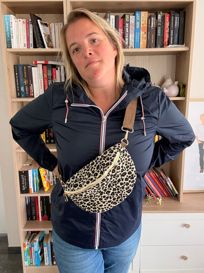 Sac Banane Velours Côtelé Imprimé Léopard – beige/noir/doré portée en ceinture par-dessus une veste sombre, bibliothèque en arrière-plan.