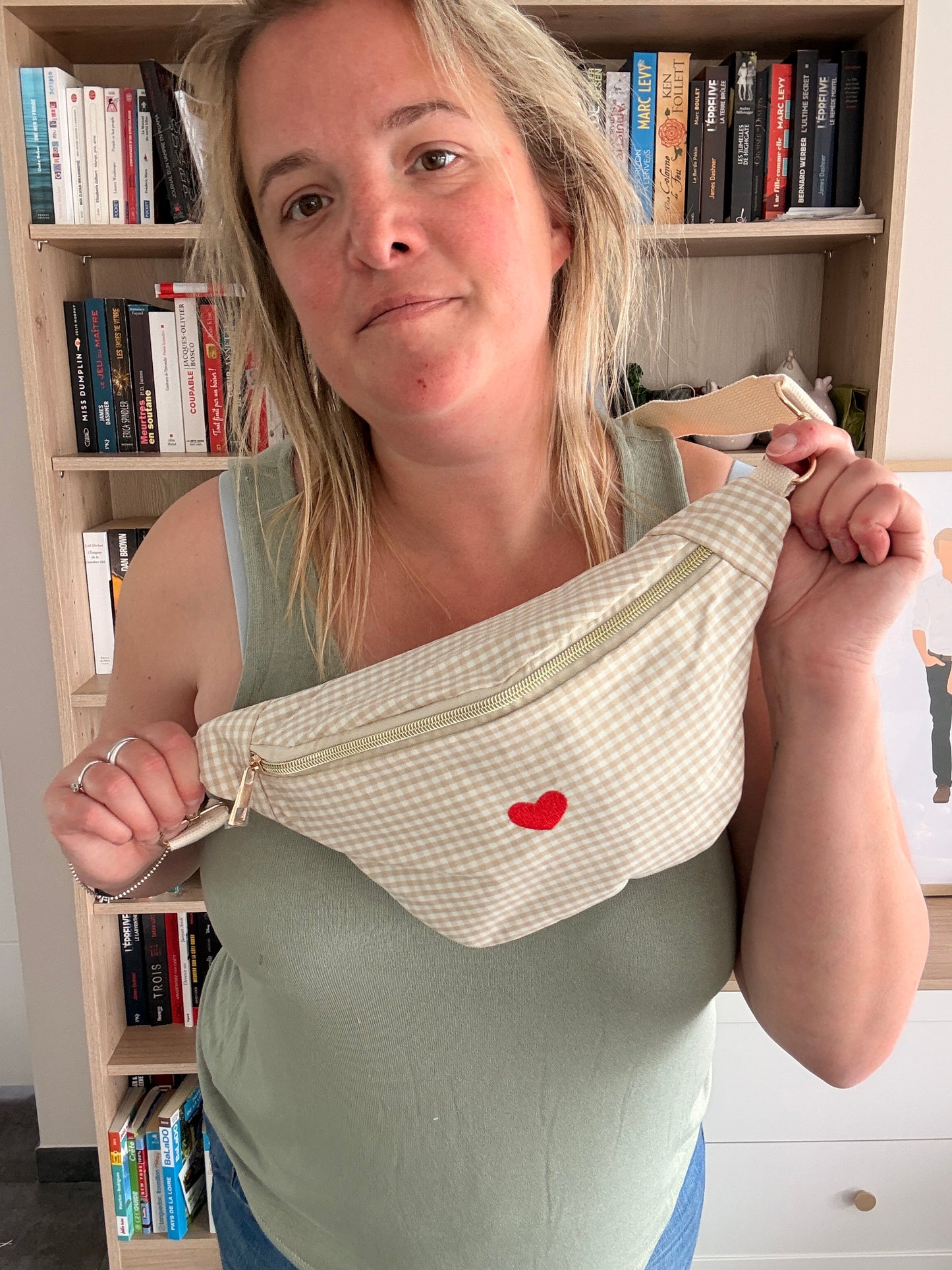 Sac banane en coton motif vichy beige et blanc avec cœur rouge, porté par une femme devant une bibliothèque.