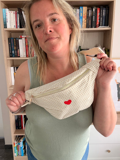 Sac banane en coton motif vichy beige et blanc avec cœur rouge, porté par une femme devant une bibliothèque.