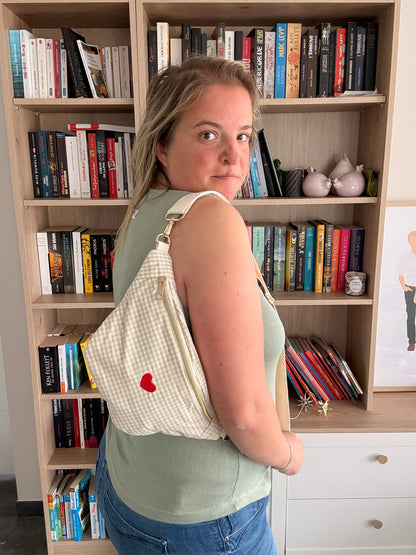 Sac banane en coton motif vichy beige et blanc avec cœur rouge portée sur l’épaule d’une femme dans une bibliothèque.