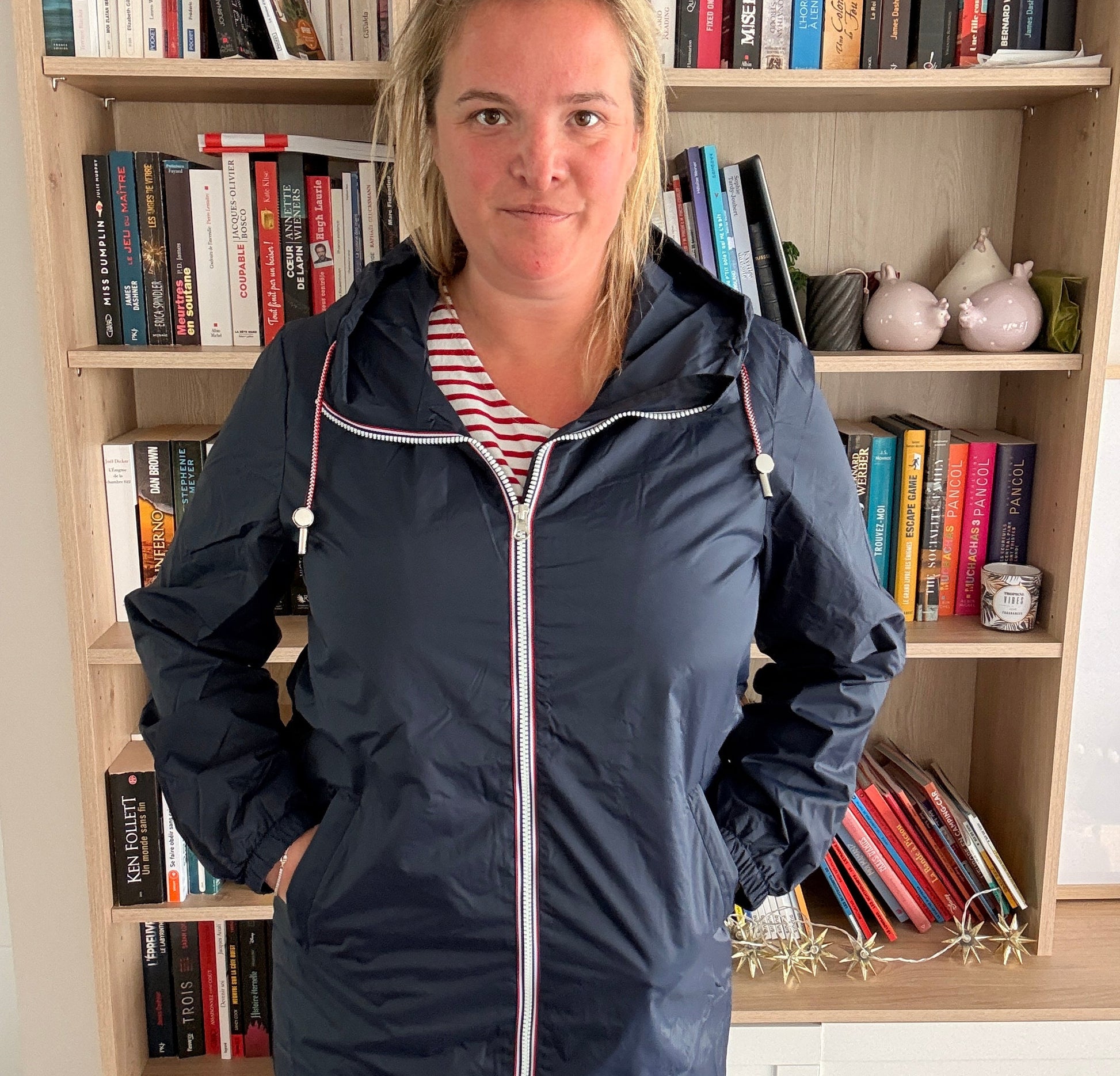 Parka manteau bleu marine imperméable Laura Jo, longueur longue, doublure fine, femme posant en intérieur devant une étagère de livres.