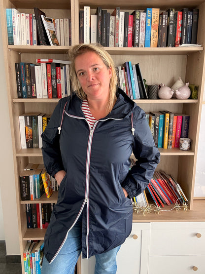 Parka bleu marine imperméable longue, doublure légère, femme debout devant une bibliothèque.