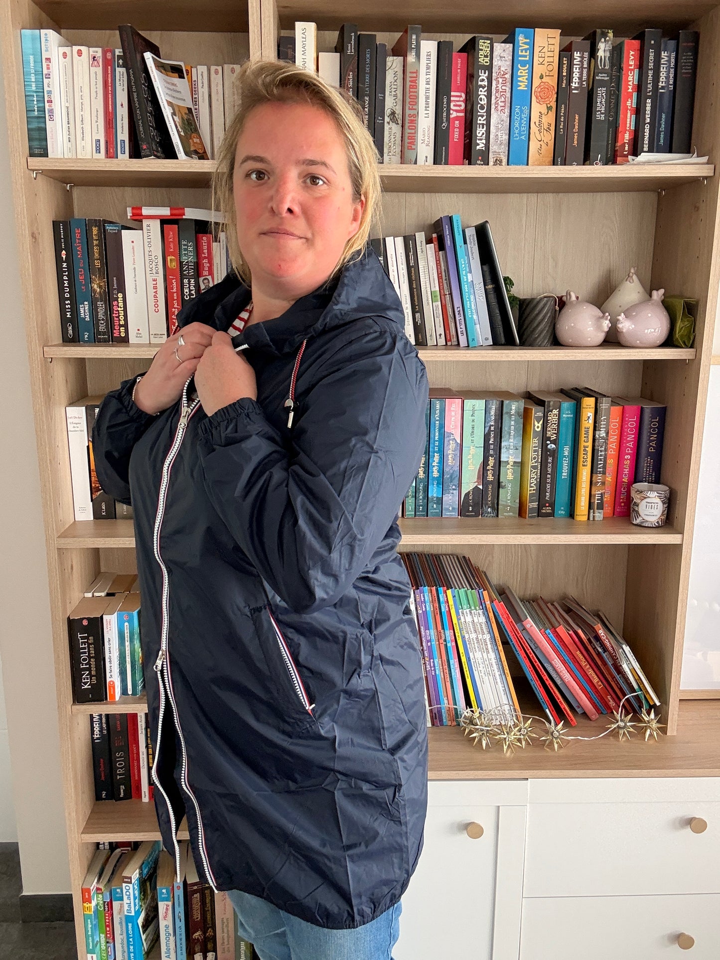 Laura Jo - Parka manteau bleu marine imperméable long avec doublure légère portée par une femme devant une bibliothèque.
