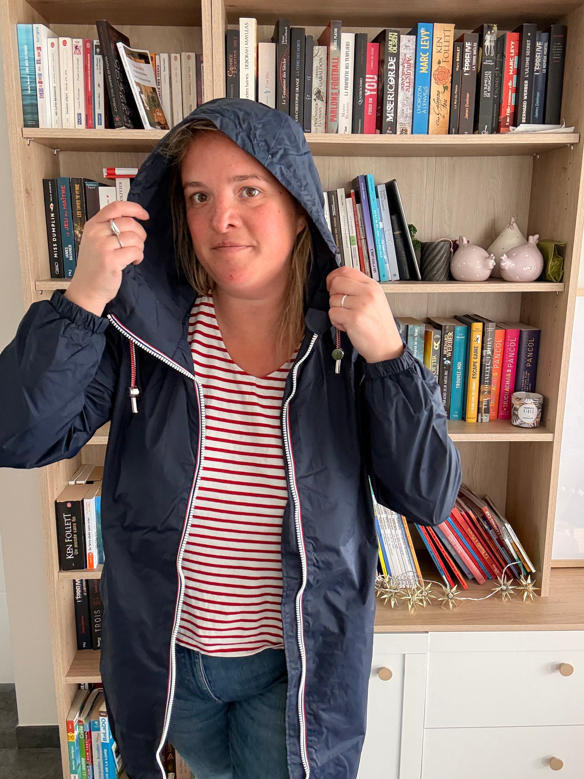 Parka manteau bleu marine imperméable longue avec doublure fine, portée par une femme dans une bibliothèque.