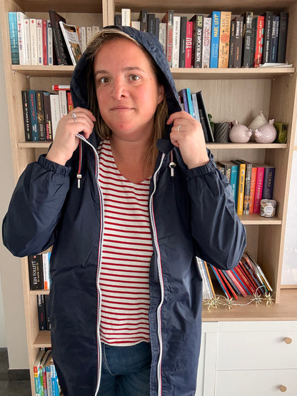 Laura Jo - Parka manteau bleu marine imperméable long avec doublure légère, femme portant capuche et fermeture éclair ouverte sur une chemise rayée à l’intérieur.