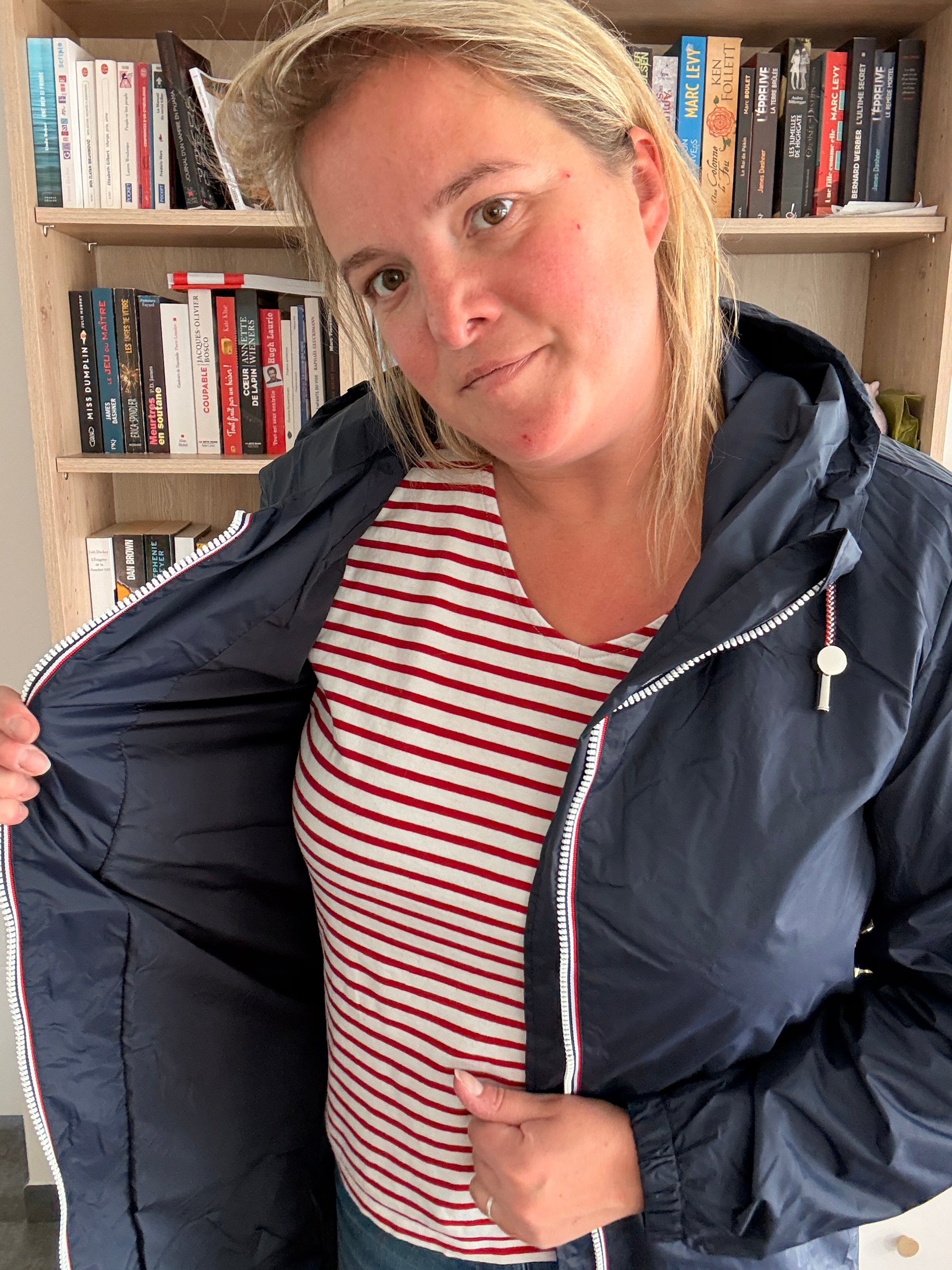 Laura Jo - Parka: manteau bleu marine imperméable long avec doublure légère, femme montrant l’intérieur cintré près d’une bibliothèque.