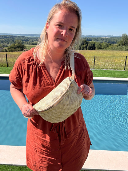 Homme ou femme portant un sac banane en paille, sur fond de piscine et paysage champêtre estival bohème. Sac banane paille femme – Style bohème été.