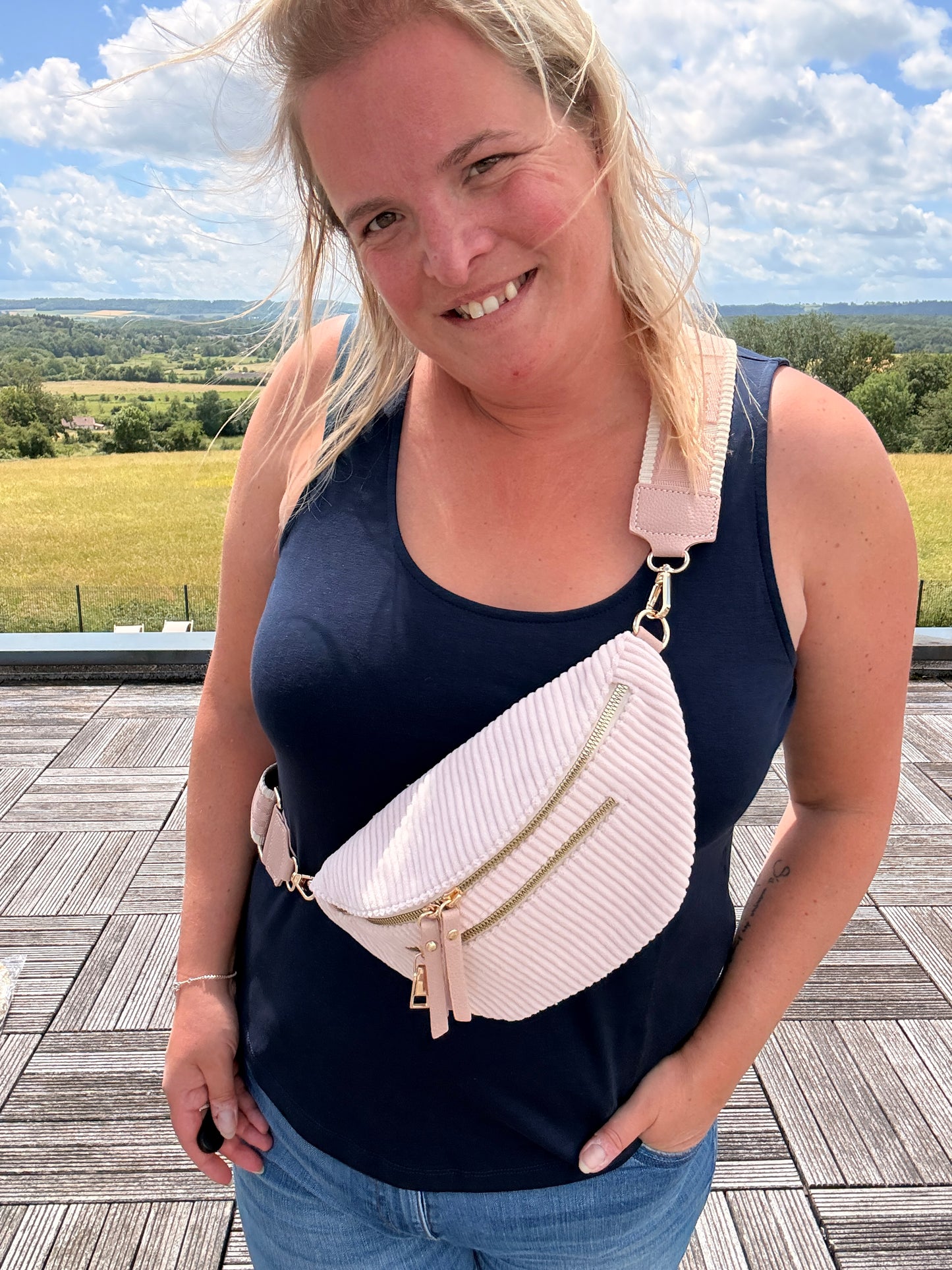 Sac banane velours côtelé rose pâle porté en bandoulière par une femme, avec deux poches zippées et sangle réglable.