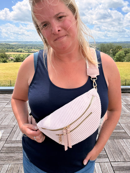 Sac banane velours côtelé rose pâle porté en bandoulière par une femme, avec deux poches zippées et sangle réglable.