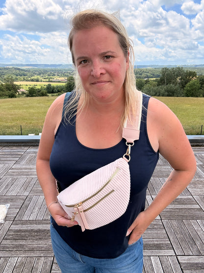 Sac banane velours côtelé femme rose pâle portée en bandoulière par une femme, deux poches zippées visibles et sangle réglable.