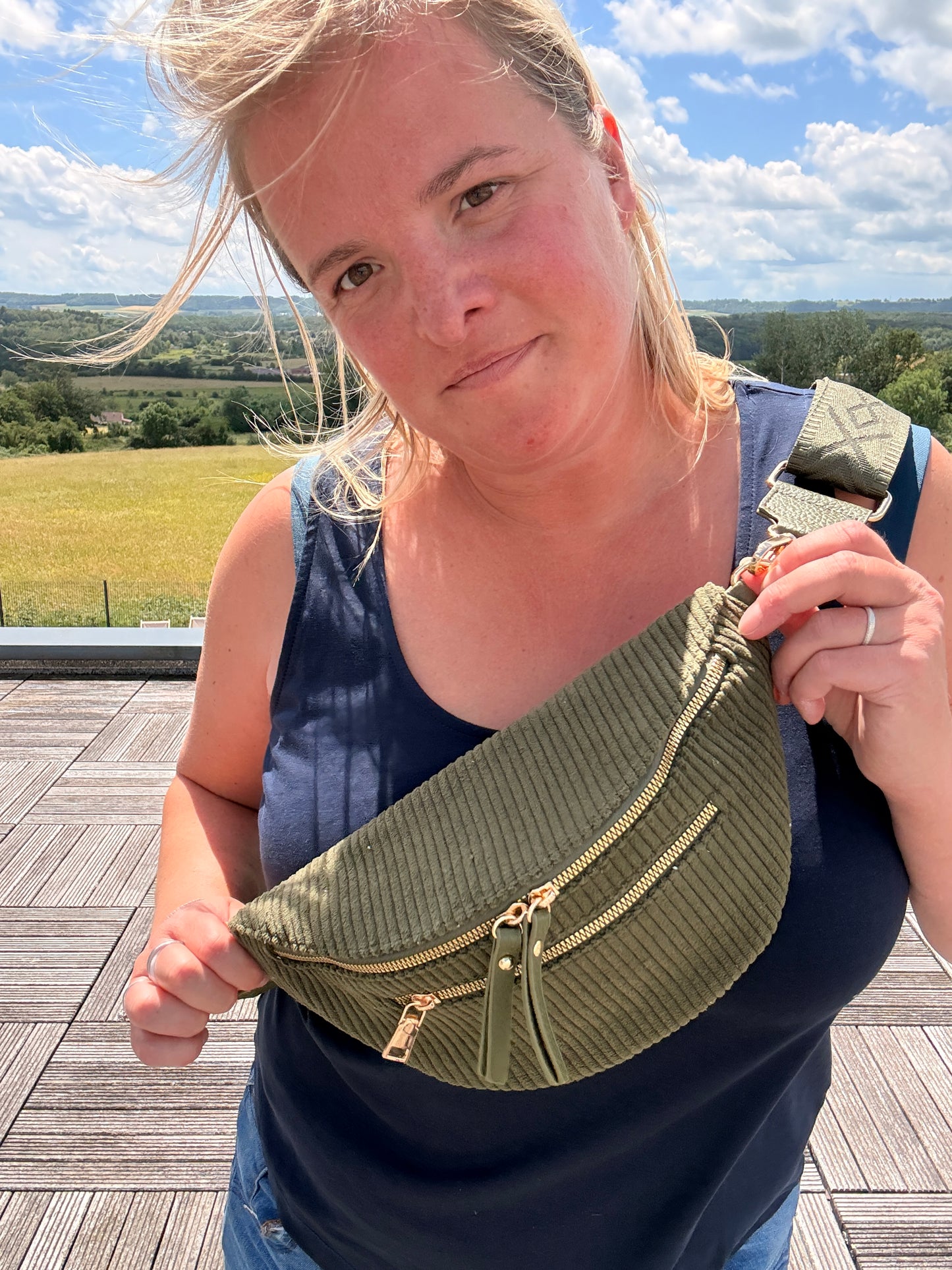 Sac banane velours côtelé kaki avec poches zippées porté en bandoulière par une femme en extérieur.