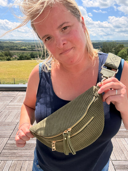 Sac banane velours côtelé kaki avec poches zippées porté sur l’épaule d’une femme en extérieur.