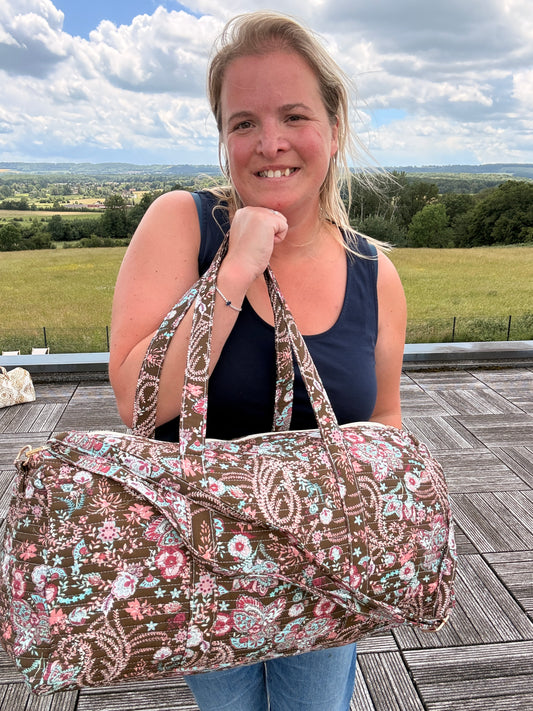 Sac polochon matelassé fleuri paisley porté par une femme, grand sac de voyage bohème chic avec bandoulière incluse, décor extérieur.