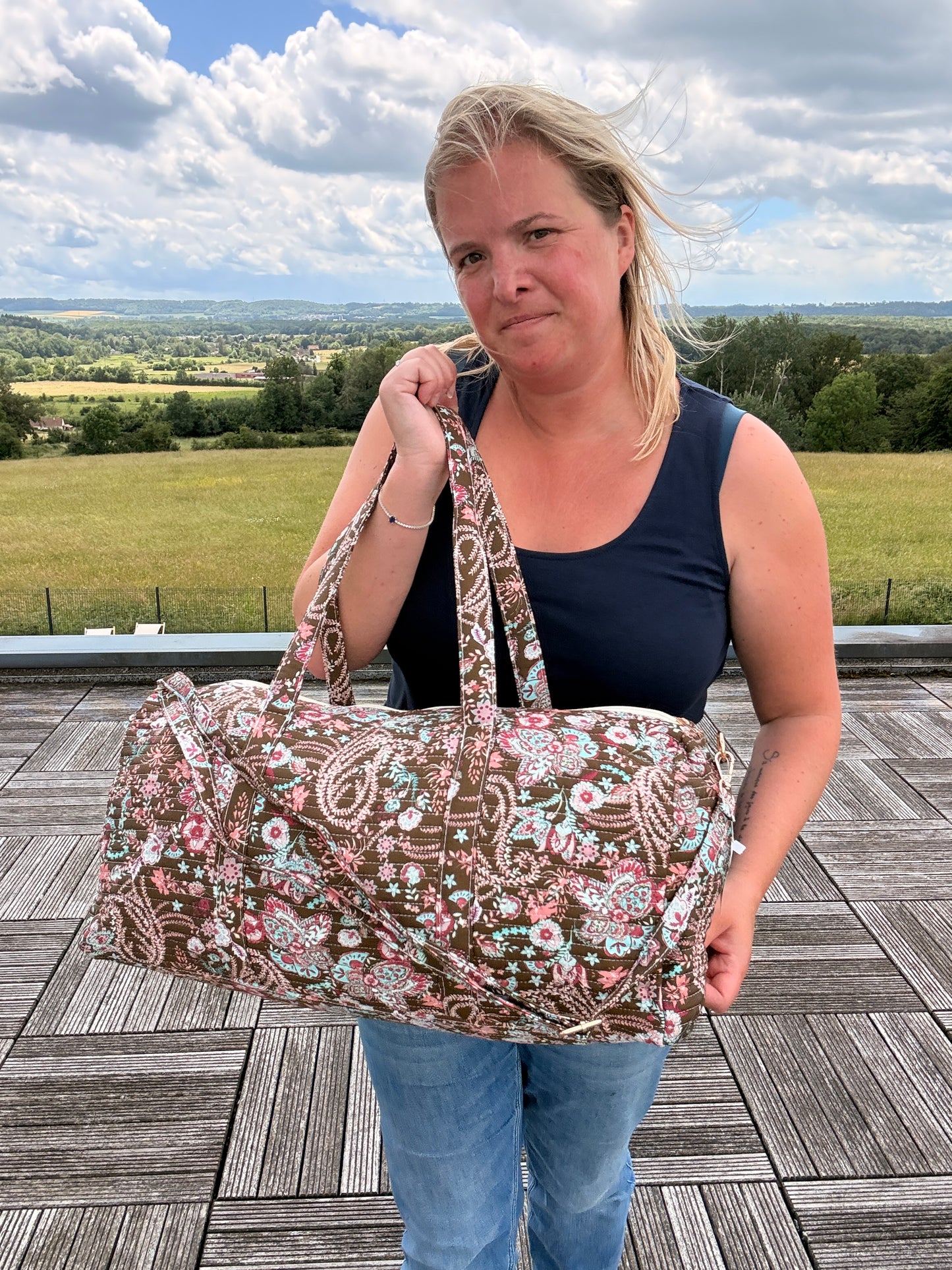 Sac polochon matelassé fleuri Paisley porté par une femme en extérieur, grand sac de voyage avec bandoulière incluse.
