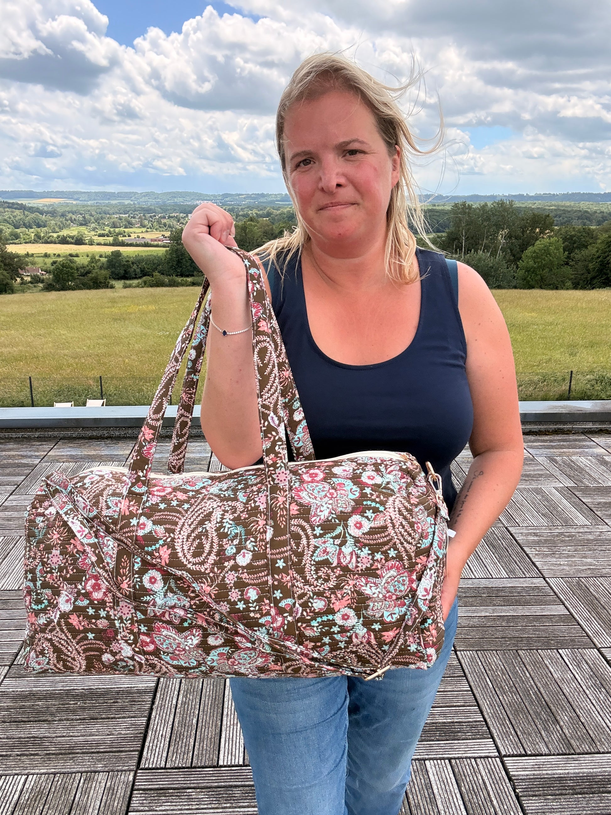 Sac polochon matelassé fleuri Paisley, grand sac de voyage femme bohème chic avec bandoulière incluse, porté par une femme en extérieur.