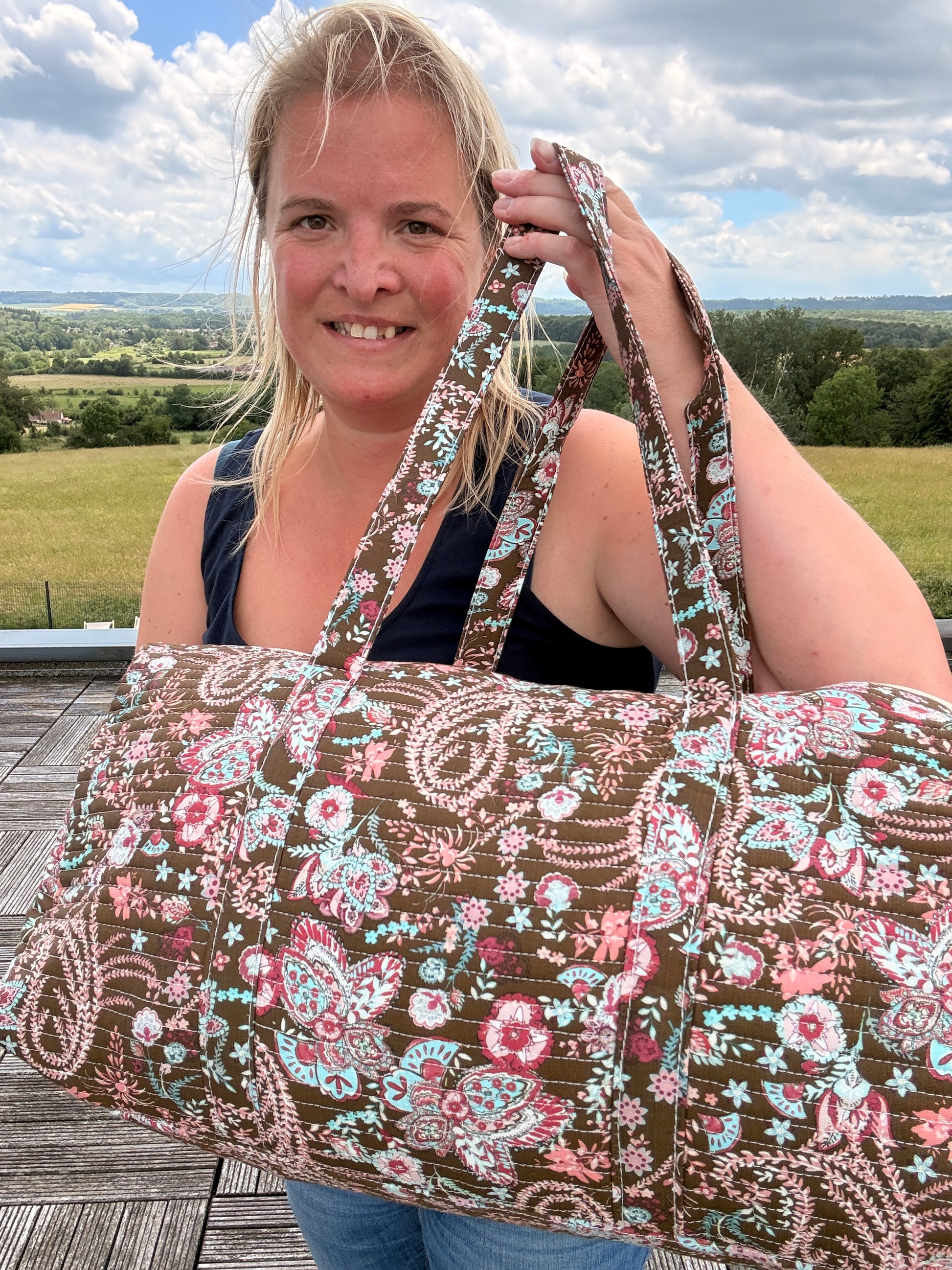 Sacs polochon matelassé fleuri paisley porté par une femme en extérieur, grand sac de voyage avec bandoulière intégrée.