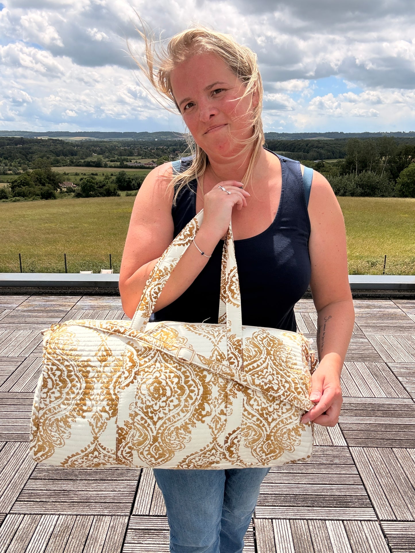 Sac polochon matelassé imprimé baroque doré porté par une femme en extérieur, style bohème chic et voyage.