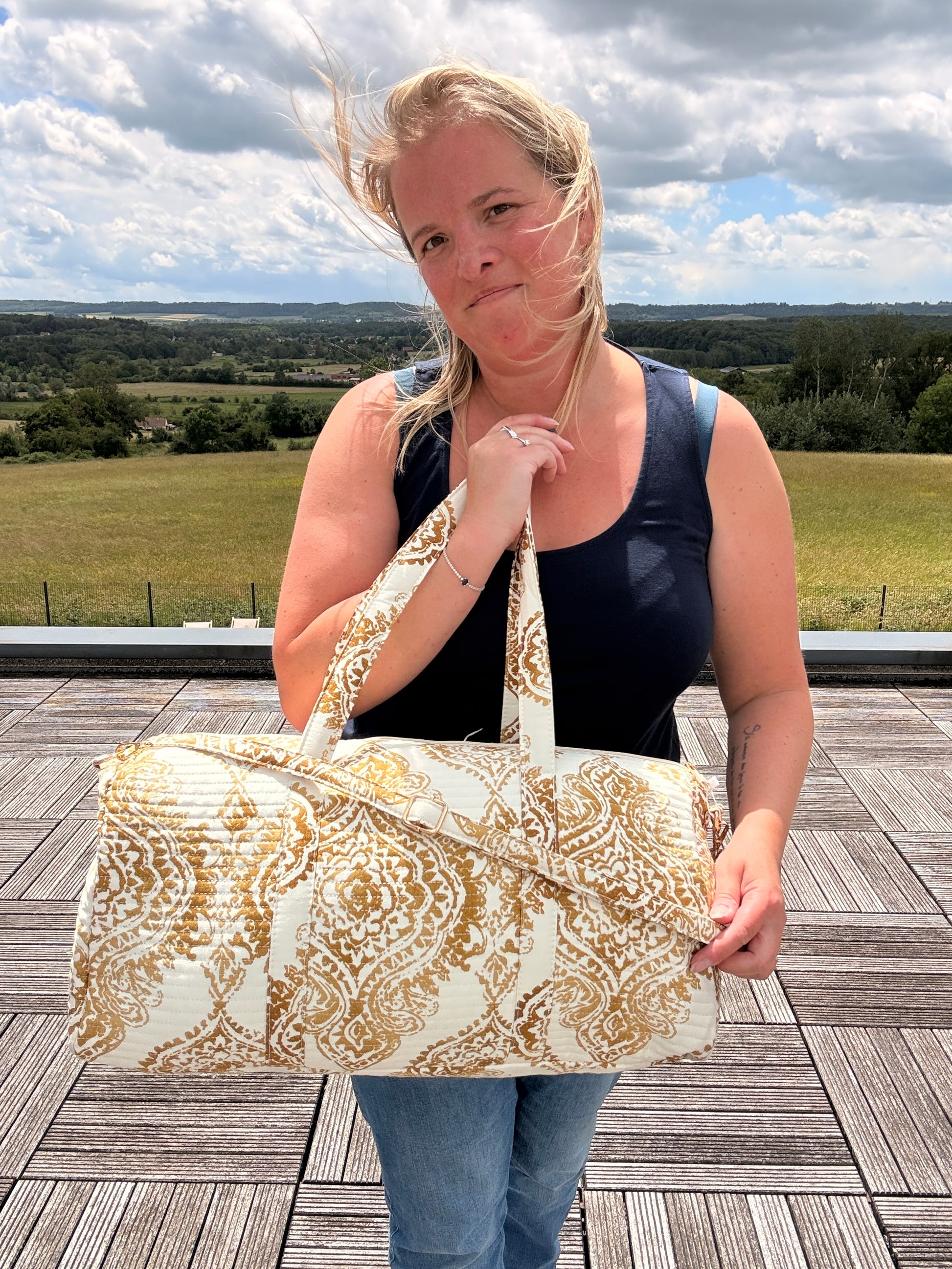 Sac polochon matelassé imprimé baroque doré porté par une femme en extérieur, style bohème chic et voyage.