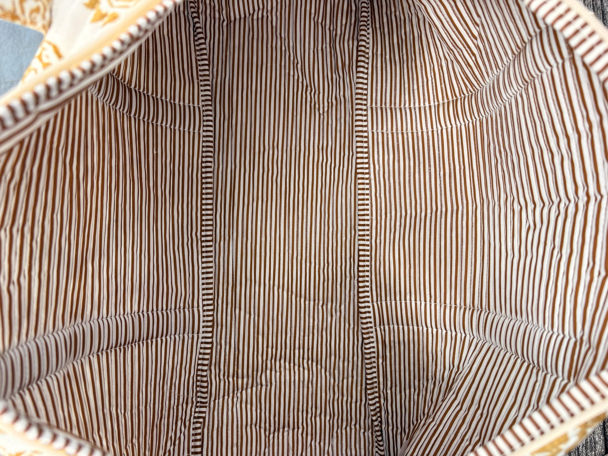 Sac polochon matelassé imprimé baroque doré vu de l’intérieur, doublure à rayures brunes et blanches.