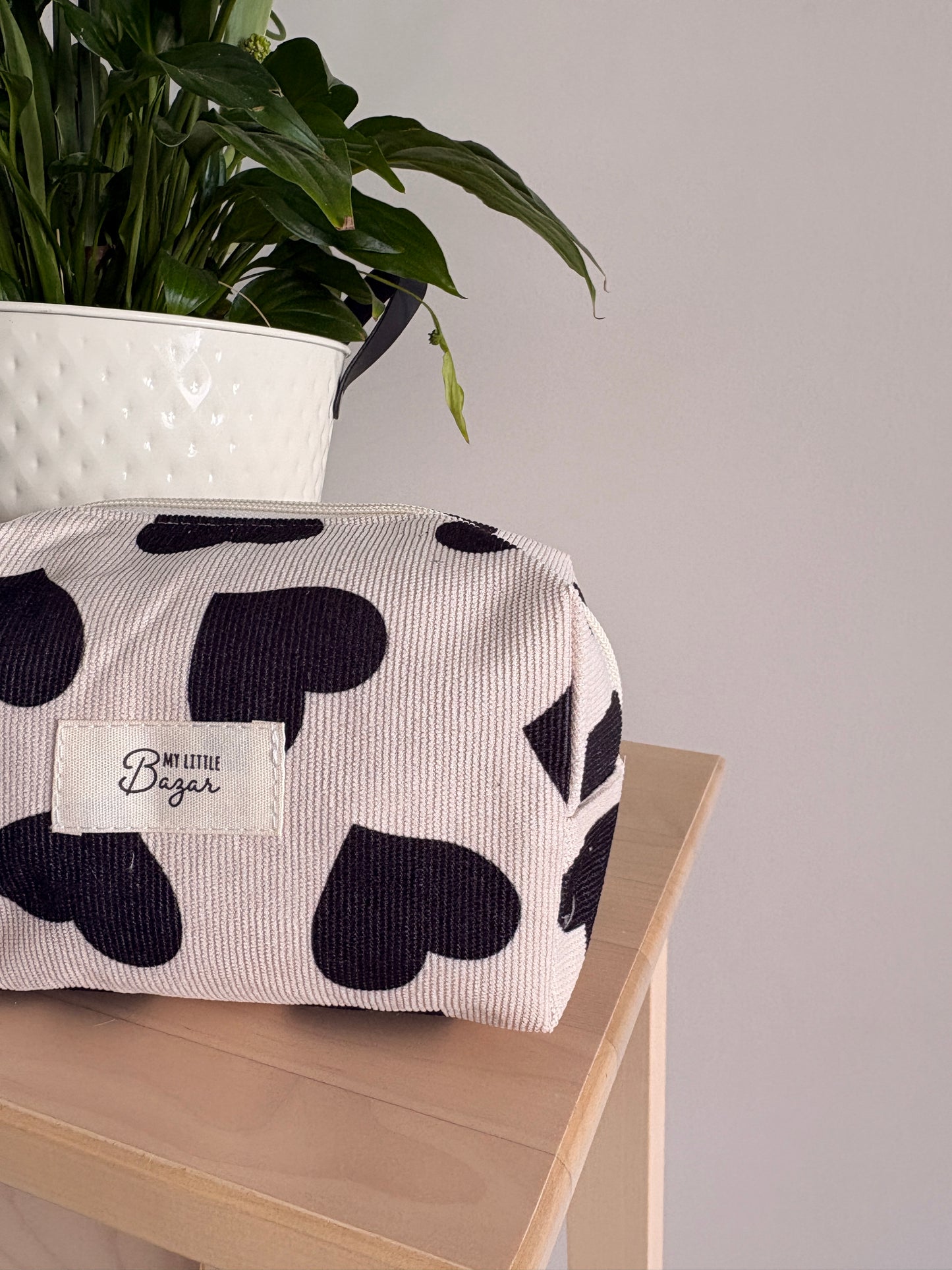 Grande trousse maquillage femme motif cœurs noirs sur table, logo « My Little Bazar » et plante en pot blanche en arrière-plan.