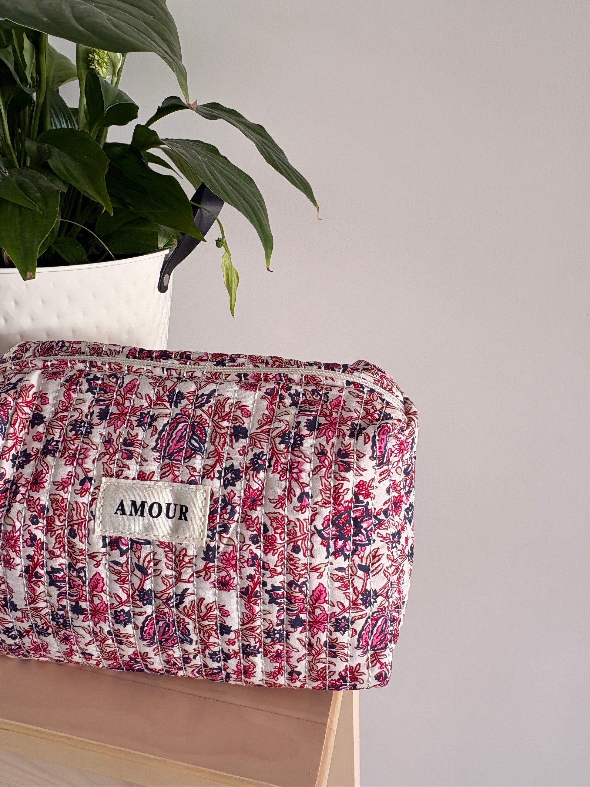 Grande trousse maquillage femme imprimé floral rose, pochette cosmétique zippée à grande capacité, posé sur meuble avec étiquette AMOUR.