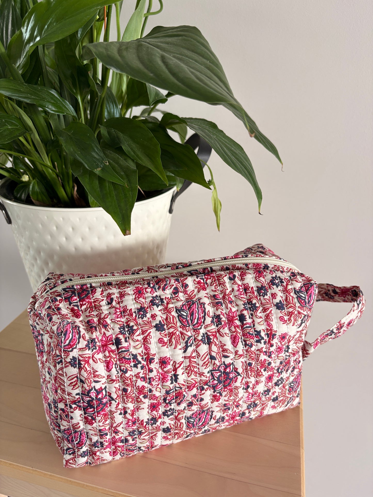 Grande trousse maquillage femme imprimé floral rose, pochette cosmétique zippée grande capacité posée près d’une plante.
