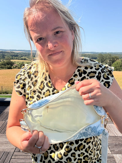 Personne tenant une pochette Sac Banane Toile de Jouy – Imprimé Bleu Turquoise ouverte pour montrer l’intérieur, en extérieur par temps ensoleillé.