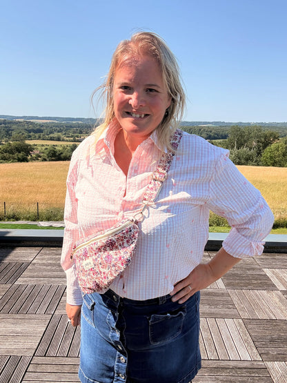 Sac banane Liberty Rose – imprimé fleuri féminine portée en bandoulière sur une blouse rose, en plein air.