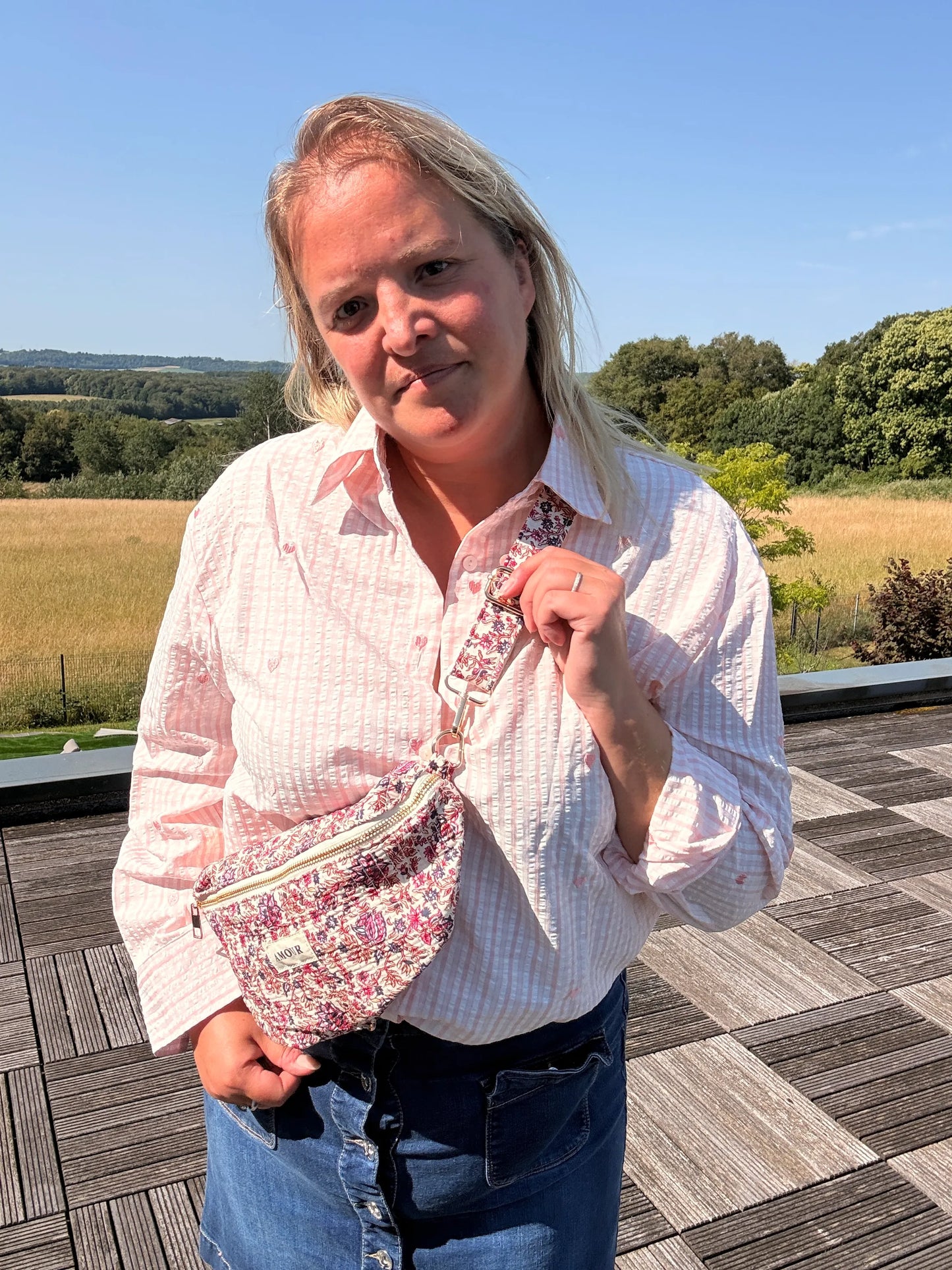 Sac banane Liberty Rose imprimé fleuri porté en bandoulière par une femme debout sur une terrasse en plein air.