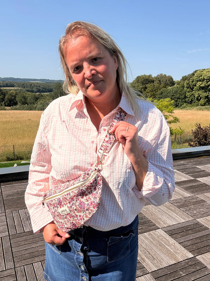 Sac banane Liberty Rose imprimé fleuri porté en bandoulière par une femme debout sur une terrasse en plein air.