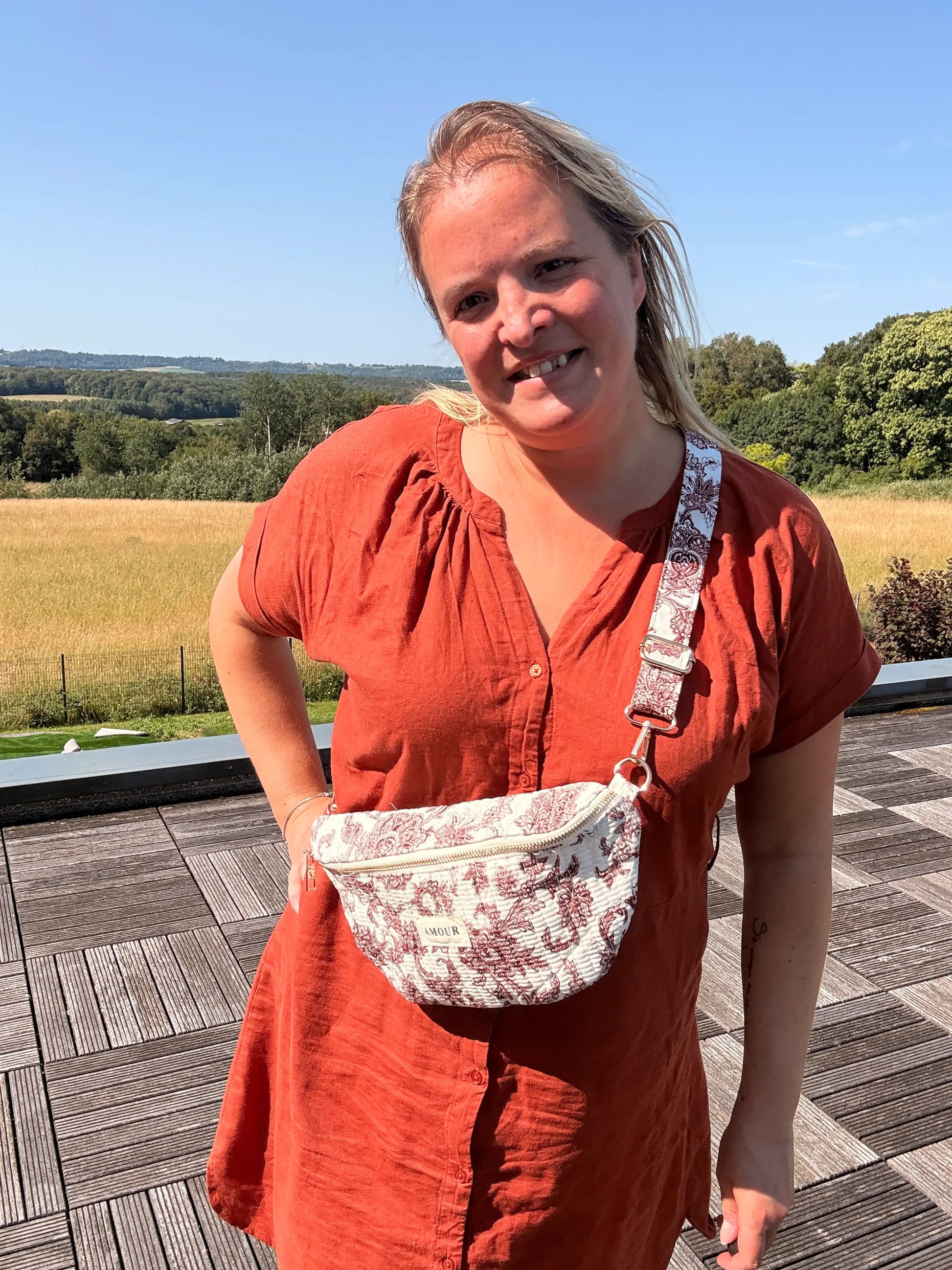 Sac banane imprimé Toile de Jouy Bordeaux porté par une femme en robe rouge, field de campagne en arrière-plan.