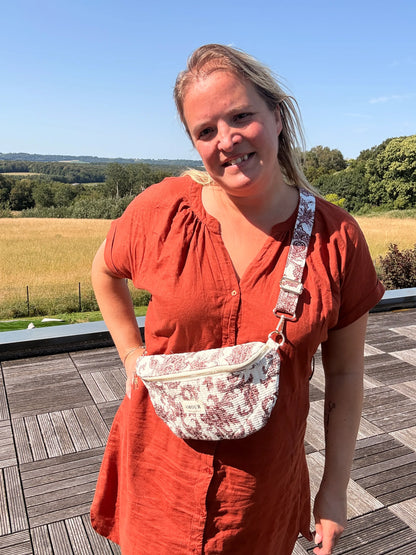 Sac banane imprimé Toile de Jouy Bordeaux porté par une femme en robe rouge, field de campagne en arrière-plan.