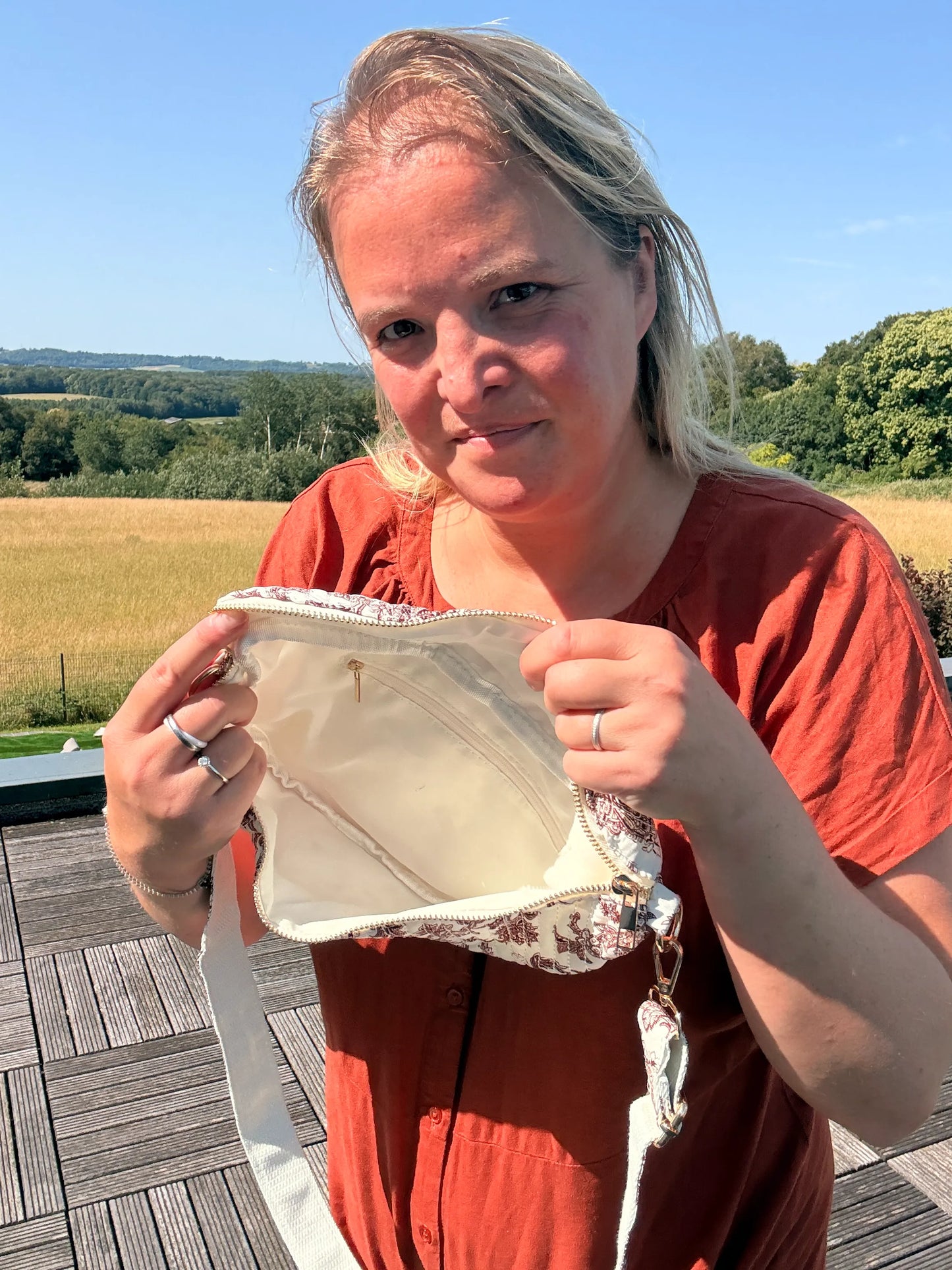 Femme tenant un sac banane en toile de Jouy Bordeaux imprimé Amour, montrant l’intérieur clair et une fermeture zippée, en extérieur.