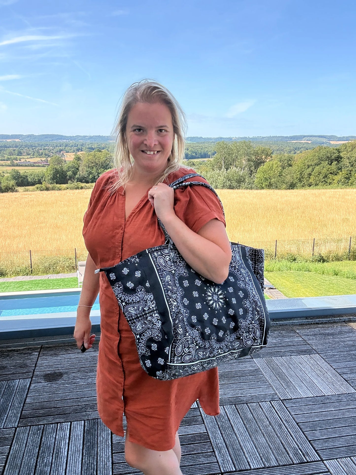 Sac polochon noir à motif Paisley porté sur l’épaule par une femme, dress orange, cadre extérieur avec champ et horizon.