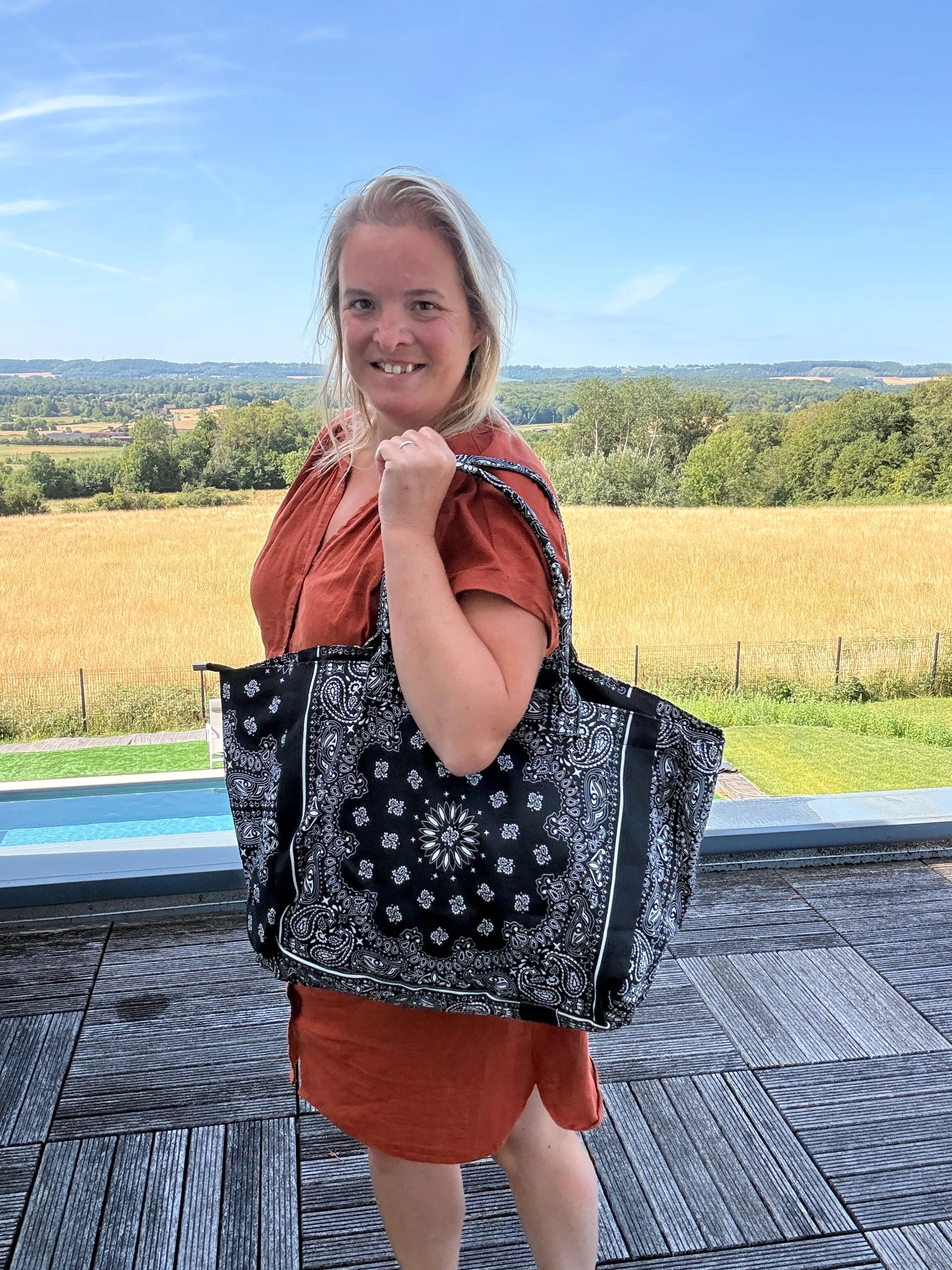 Sac polochon noir à motif cachemire porté sur l’épaule par une femme lors d’une promenade extérieure.