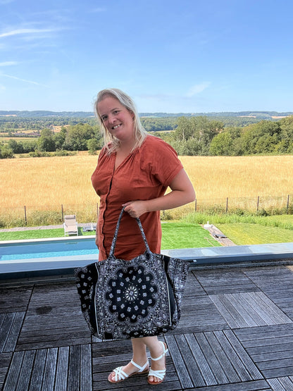 Sac polochon é shoulder en coton paisley noir grand format zippé, porté par une femme devant une vue champêtre.