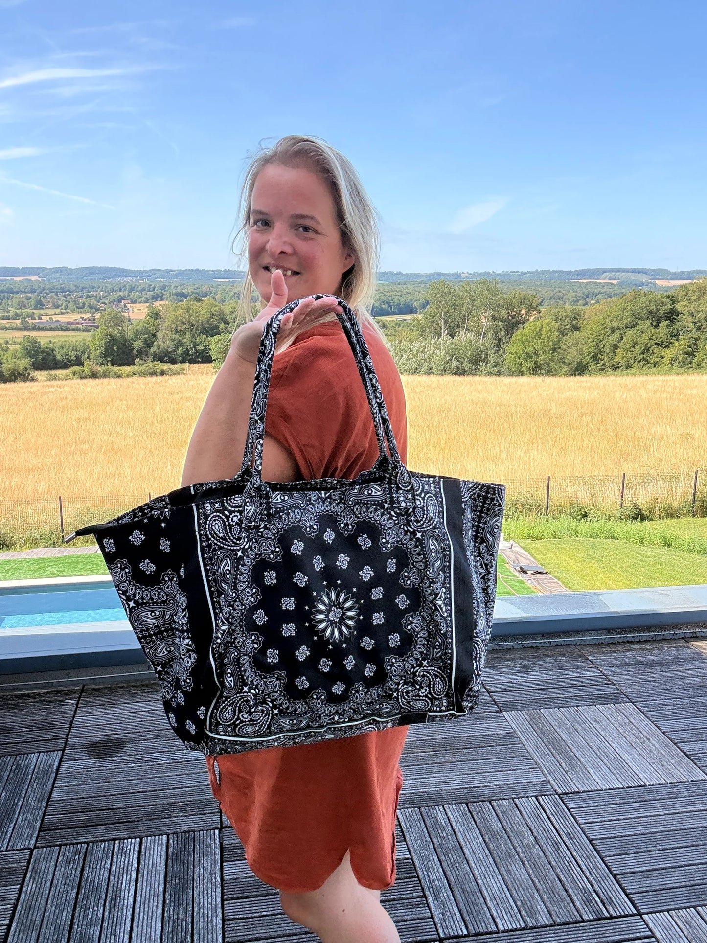 Sac polochon épaule noir et blanc à motif paisley, porté par une femme en robe orange, en extérieur. Grand format zippé.