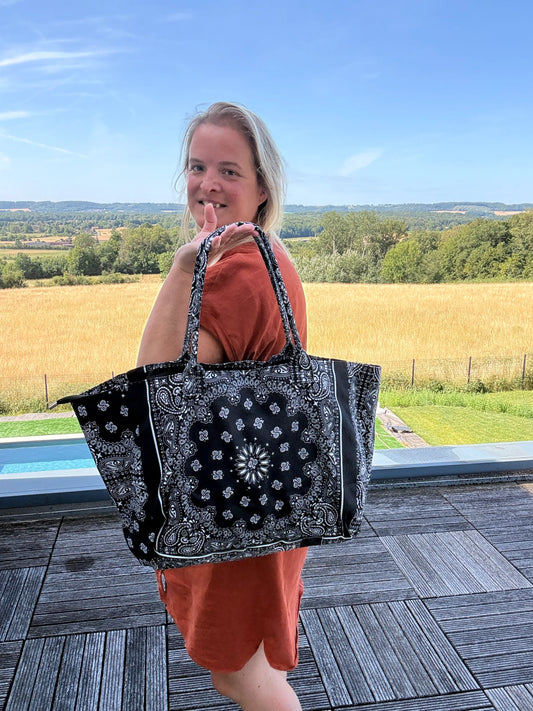 Sac polochon épaule noir et blanc à motif paisley, porté par une femme en robe orange, en extérieur. Grand format zippé.