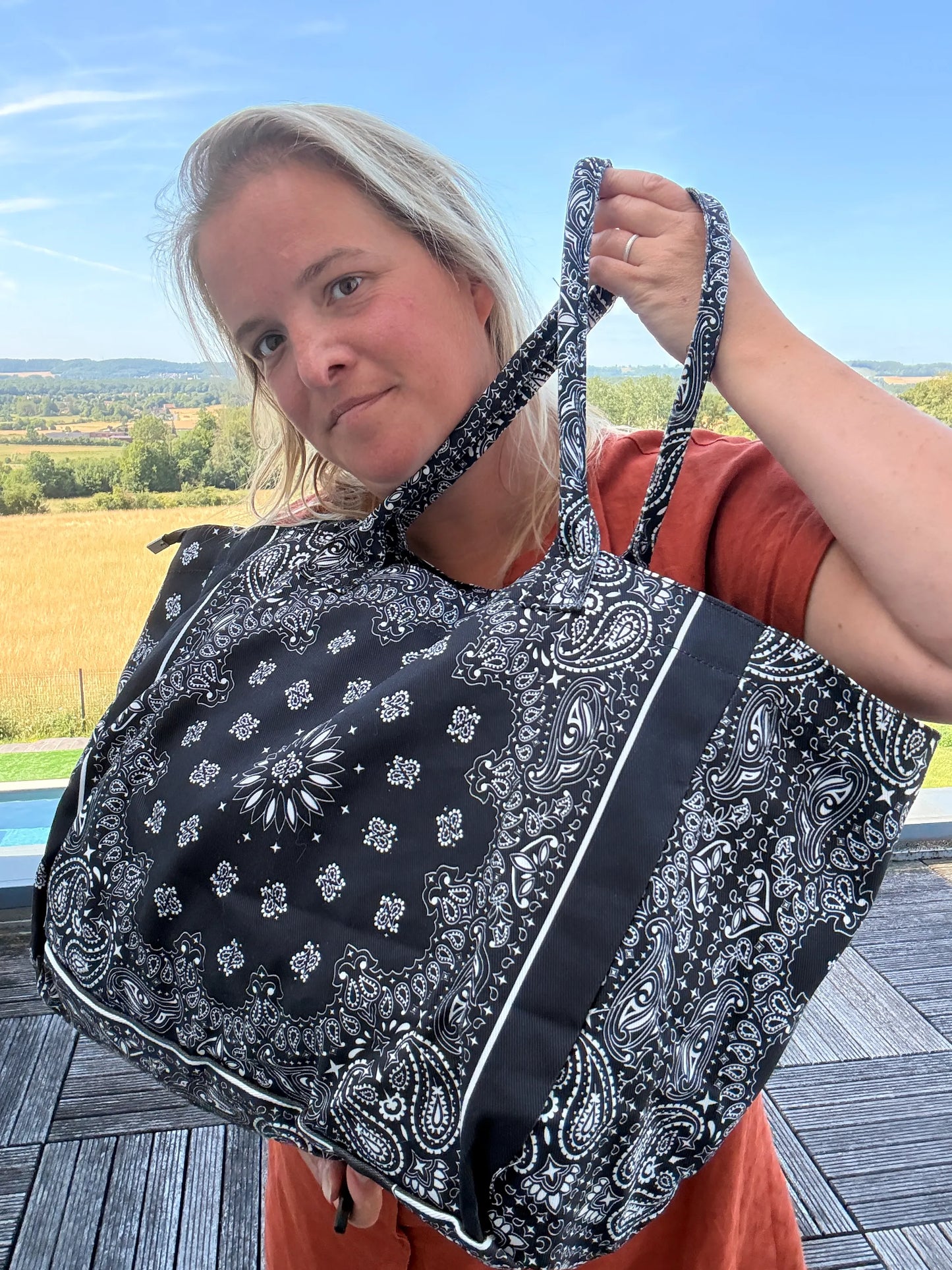 Sac polochon à motif bandana noir et blanc, doublé, grand format, porté sur l’épaule par une femme sur terrasse extérieur.