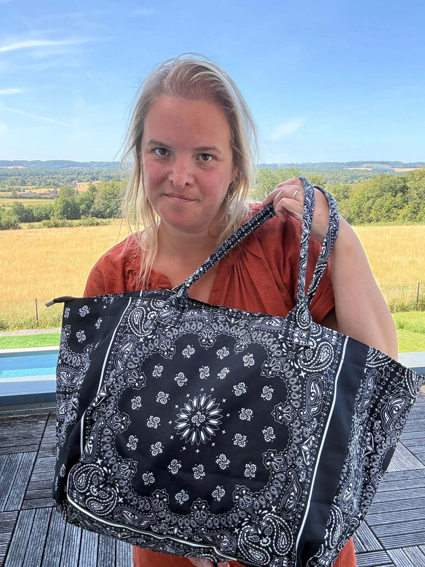 Femme tenant un grand sac polochon noir à motif bandana paisley, zippé, en coton, sur balcon face à campagne.