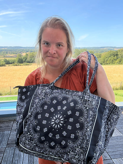 Femme tenant un grand sac polochon noir à motif bandana paisley, zippé, en coton, sur balcon face à campagne.